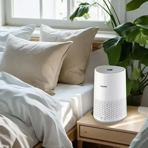 Purificateur d'air connecté Philips AC0651/10 posé sur une table de chevet dans une chambre lumineuse avec plantes et literie claire
