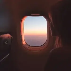 Voyager sans dérégler son sommeil : guide complet lumière et décalage horaire Voyageuse observant le lever du soleil depuis un hublot d’avion, symbole d’adaptation du sommeil et du rythme circadien en voyage.