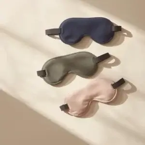 Masque de sommeil pas cher : quand un modèle à petit prix peut suffire ? Masque de sommeil pas cher de qualité en bleu marine et beige posé sur linge naturel avec éclairage doux, illustrant les critères de choix pour moins de 10 euros