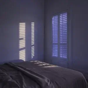 Pollution lumineuse : quand la lumière artificielle s’invite dans votre sommeil Chambre au crépuscule avec lumière extérieure filtrant à travers les volets, illustrant la pollution lumineuse nocturne qui perturbe le sommeil