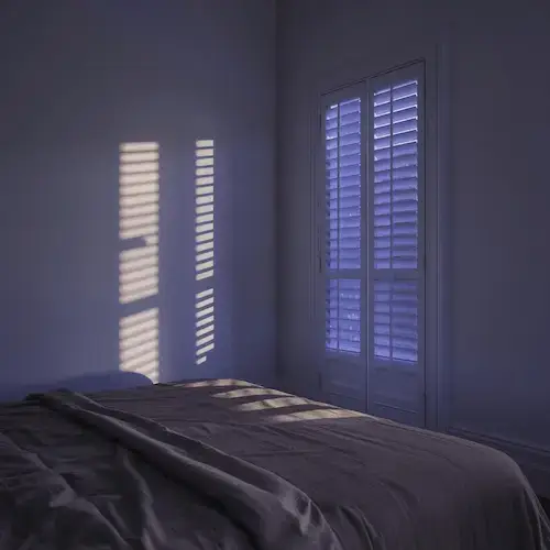 Chambre au crépuscule avec lumière extérieure filtrant à travers les volets, illustrant la pollution lumineuse nocturne qui perturbe le sommeil