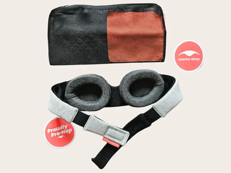 Manta Sleep Mask Original avec sa pochette de transport en mesh noir et corail, montrant le masque avec coques grises et bande ajustable