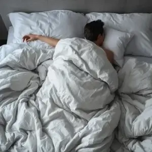 Trop chaud au lit : les erreurs fréquentes qui aggravent l'inconfort Personne dormant avec le bras hors de la couette illustrant une sensation de trop chaud au lit et une surchauffe du couchage