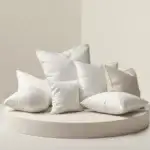 Meilleurs oreillers Dodo : comparatif des modèles ergonomiques et mémoire de forme Sélection de plusieurs oreillers blancs élégants disposés sur un socle beige clair pour illustrer un comparatif d’oreillers Dodo