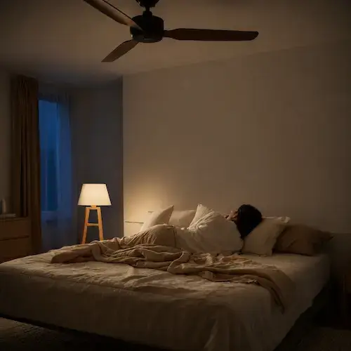 Personne allongée dans une chambre la nuit sous un ventilateur de plafond, illustrant le besoin de bruit pour dormir