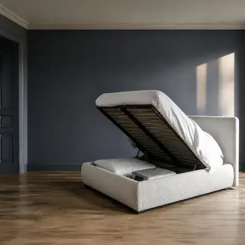 Lit coffre en bouclette écru au sommier relevé, coffre de rangement ouvert avec couette et valise, chambre au mur bleu nuit